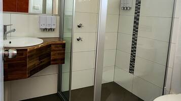 Ein modernes Badezimmer mit einer Duschkabine aus Glas, einem Holzboden, einem weißen Waschbecken und einer Toilette.