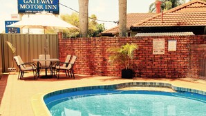 A pool area with a brick wall, a table with chairs, and a sign for Gateway Motor Inn. - Childers Gateway Motor Inn (Childers)