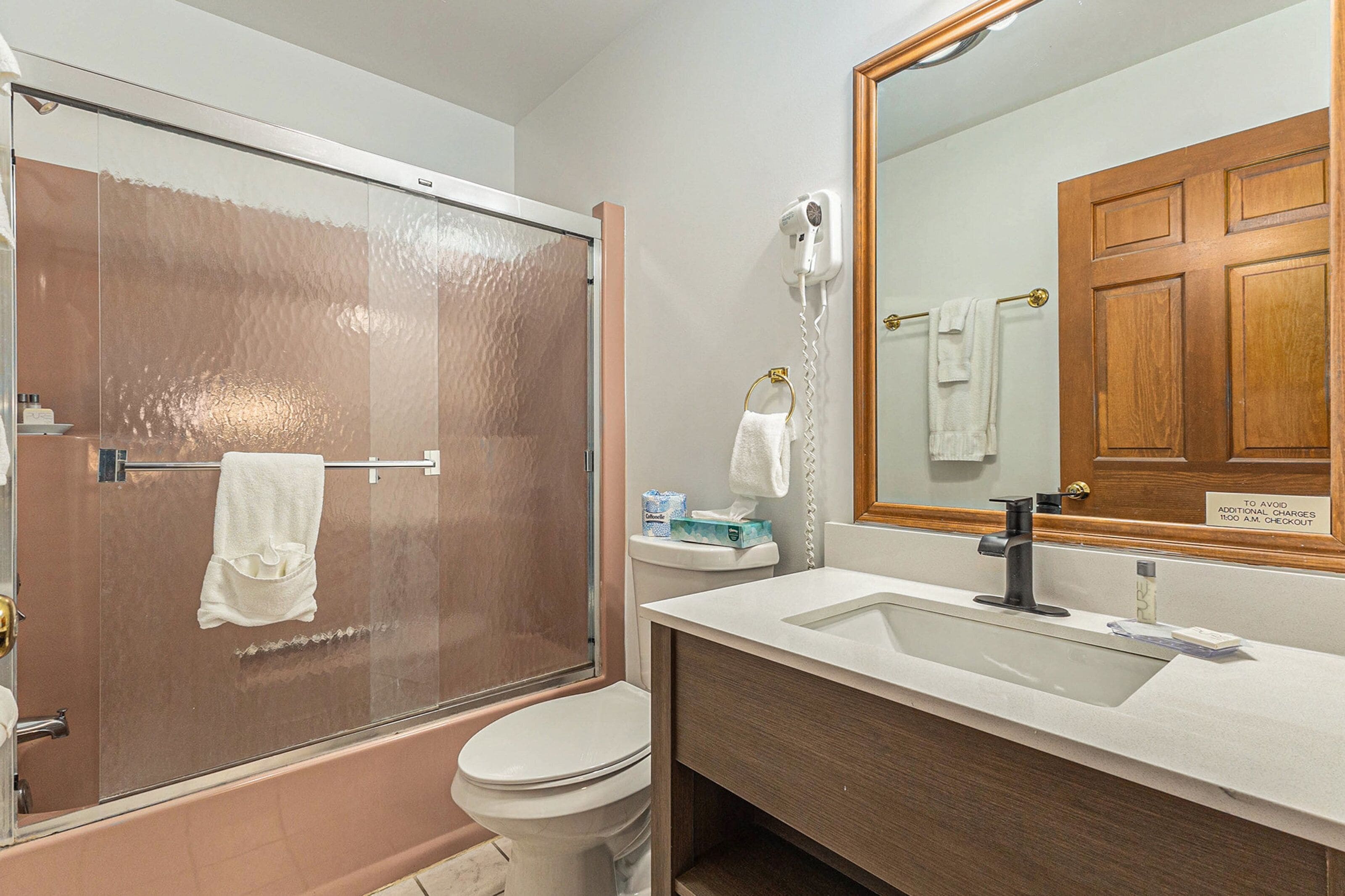 A bathroom with a glass-enclosed shower, a white toilet, a sink with a mirror, and a towel rack.