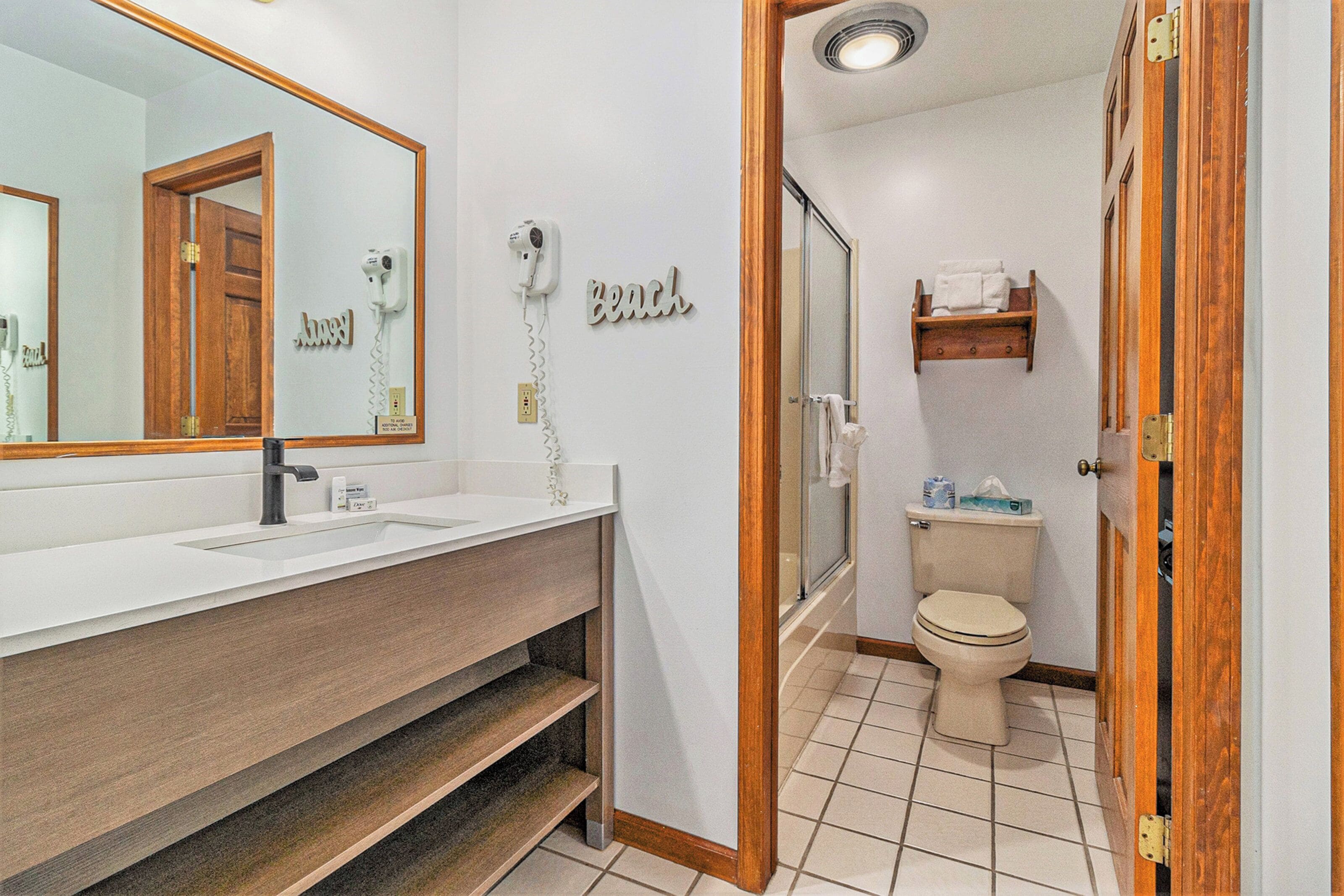 Un bagno con mobile lavabo in legno, uno specchio grande, un asciugacapelli, un water e una doccia.