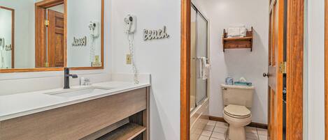 A bathroom with a wooden vanity, a large mirror, a hairdryer, a toilet, and a shower area.