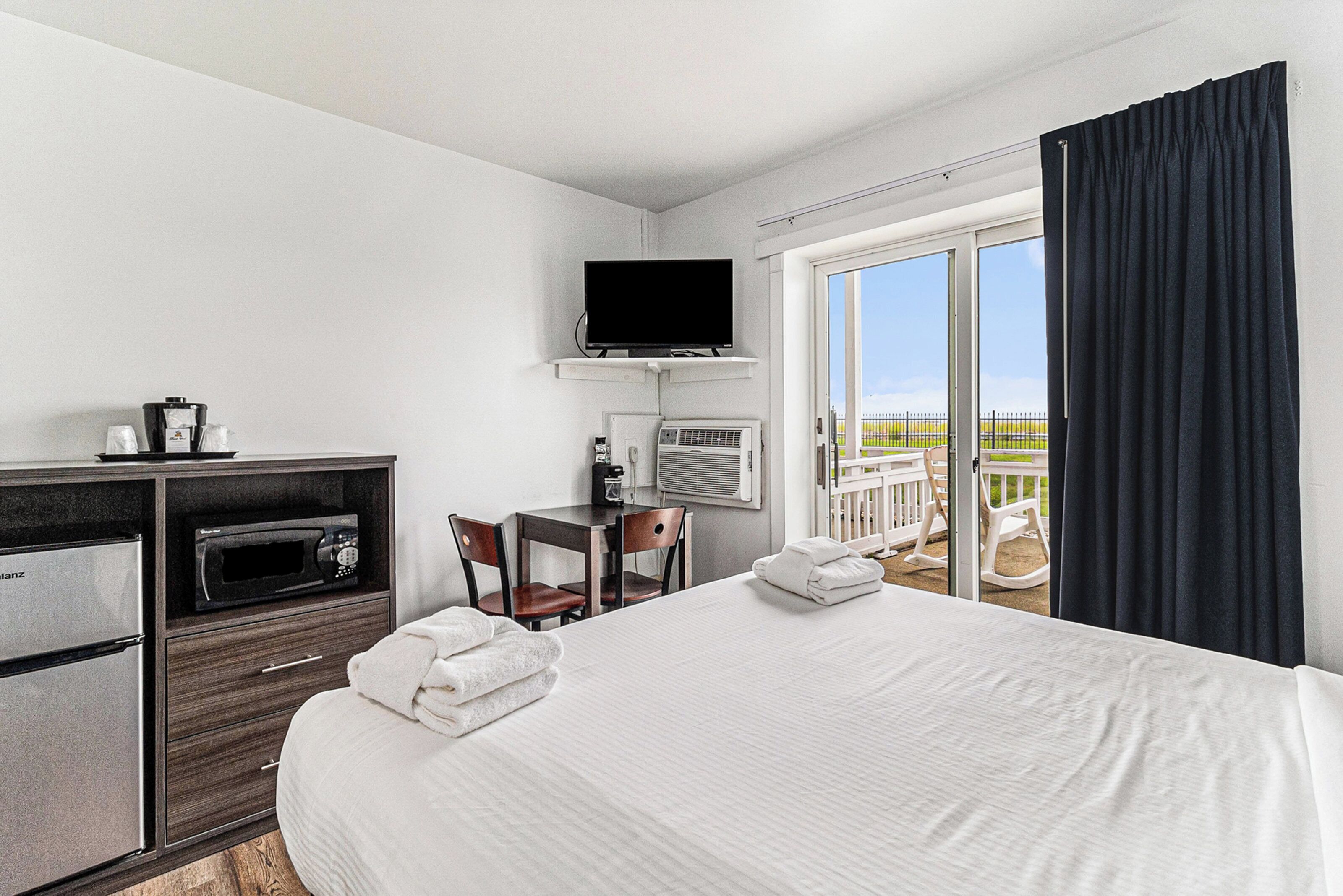 Habitación de hotel con cama, escritorio con televisor, microondas y refrigerador. Balcón con vista al paisaje.