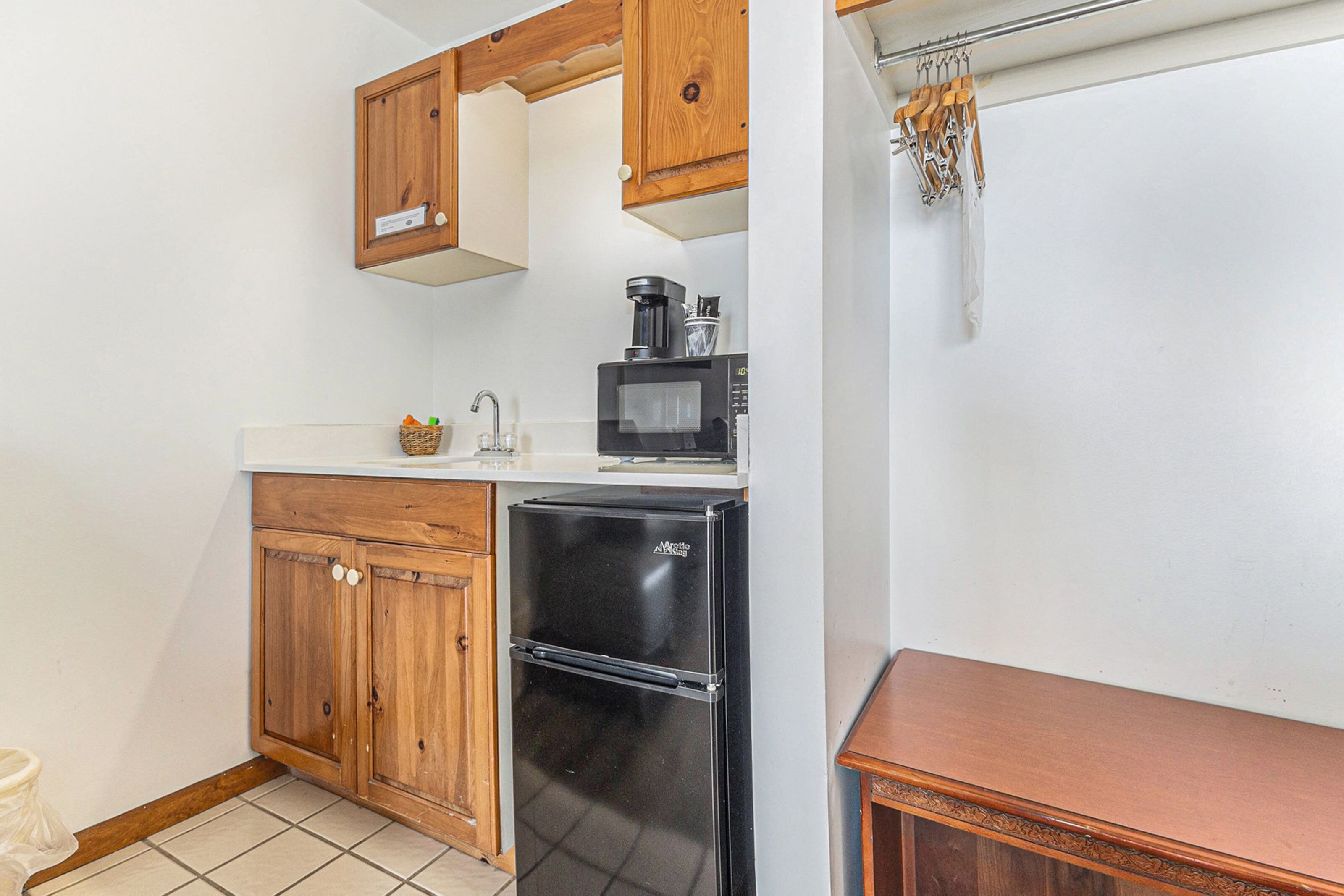A compact kitchen with wooden cabinets, a black refrigerator, a microwave, and a small countertop.