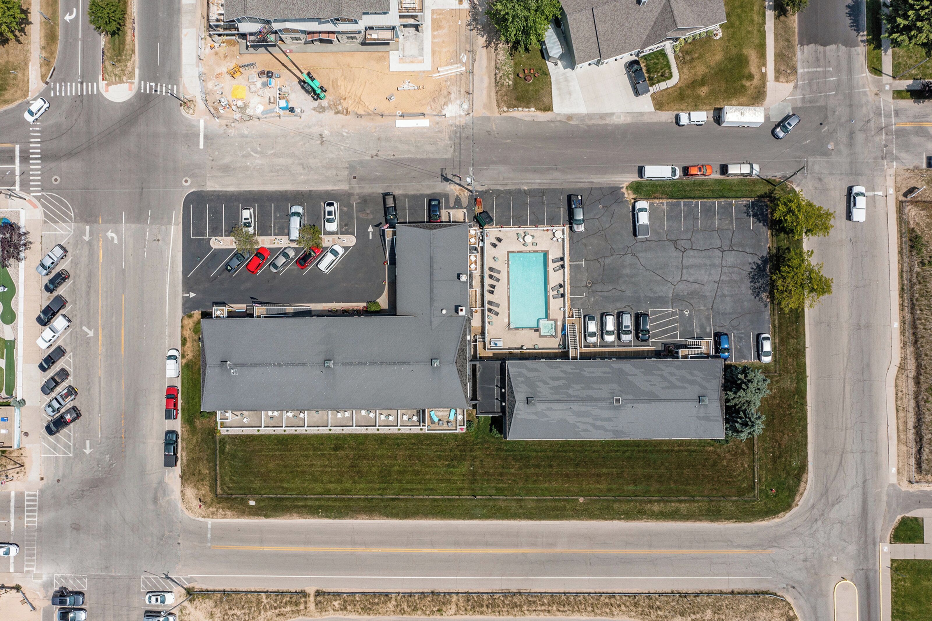 Vista aérea de un estacionamiento con varios coches, una piscina y un edificio de techo plano.