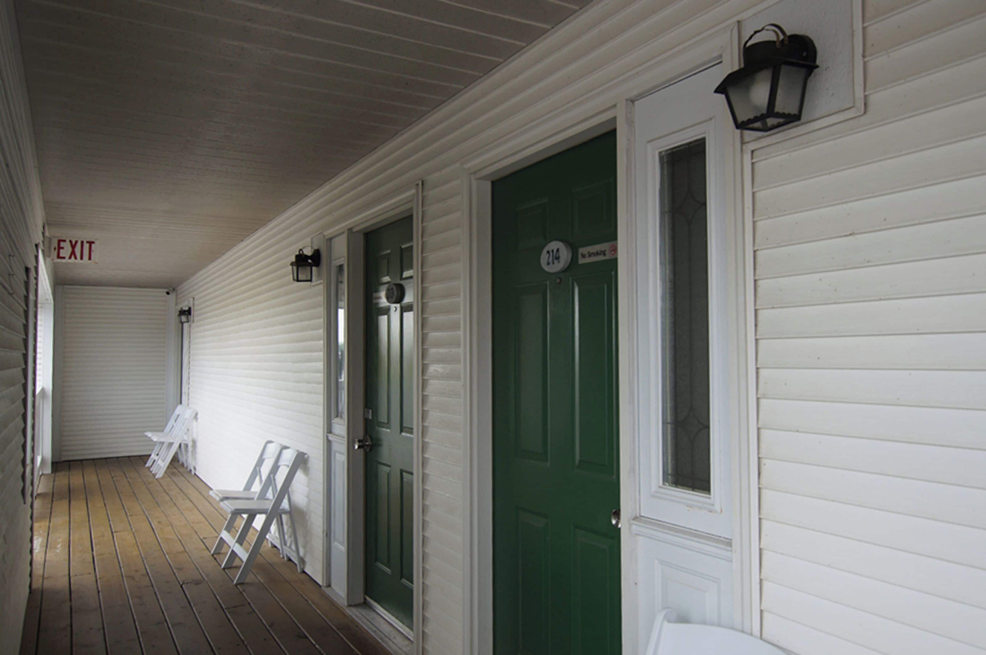 A covered porch with white siding, a green door labeled "214," and two white chairs.