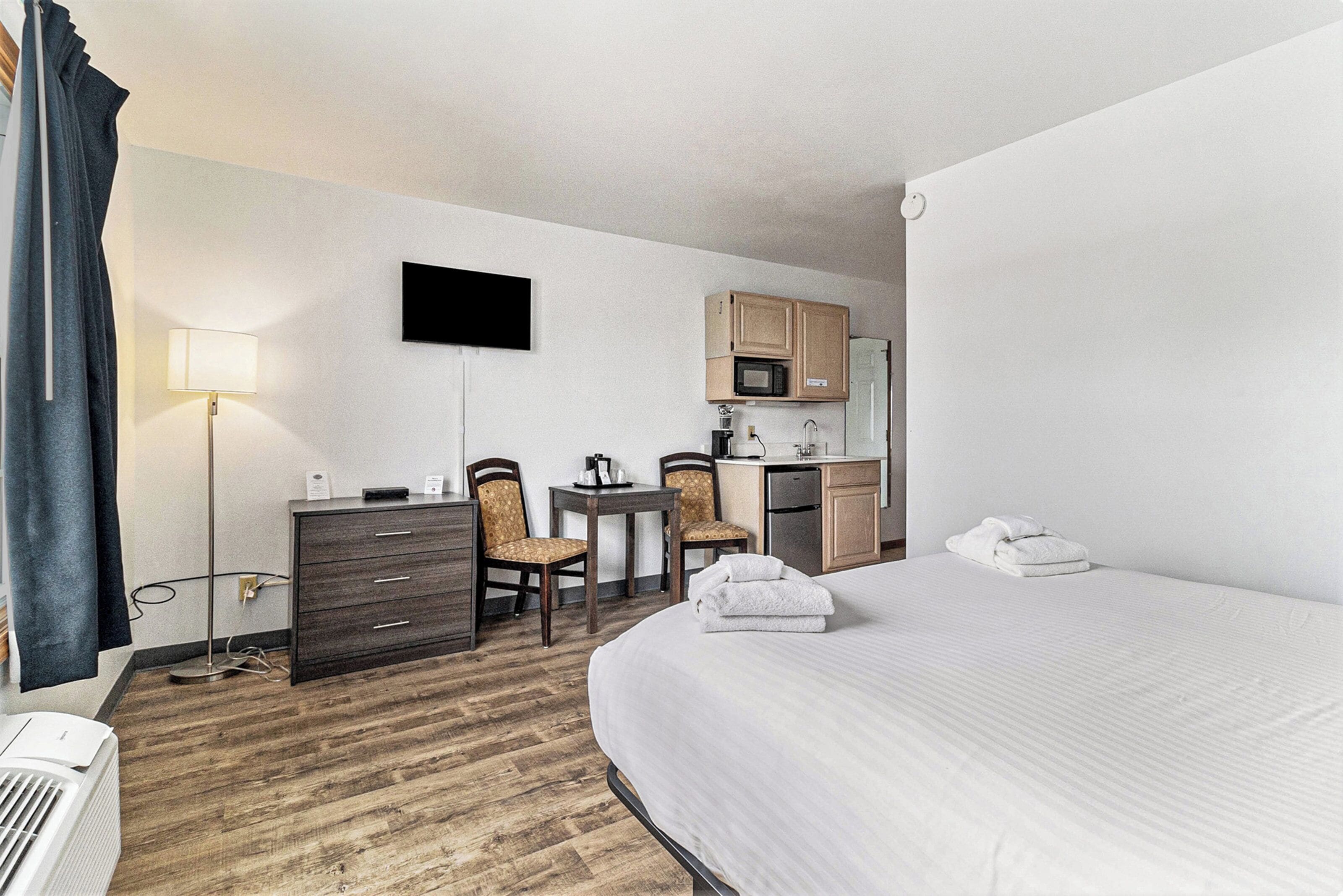 Een hotelkamer met een bed, een bureau met stoelen, een magnetron en een televisie aan de muur.