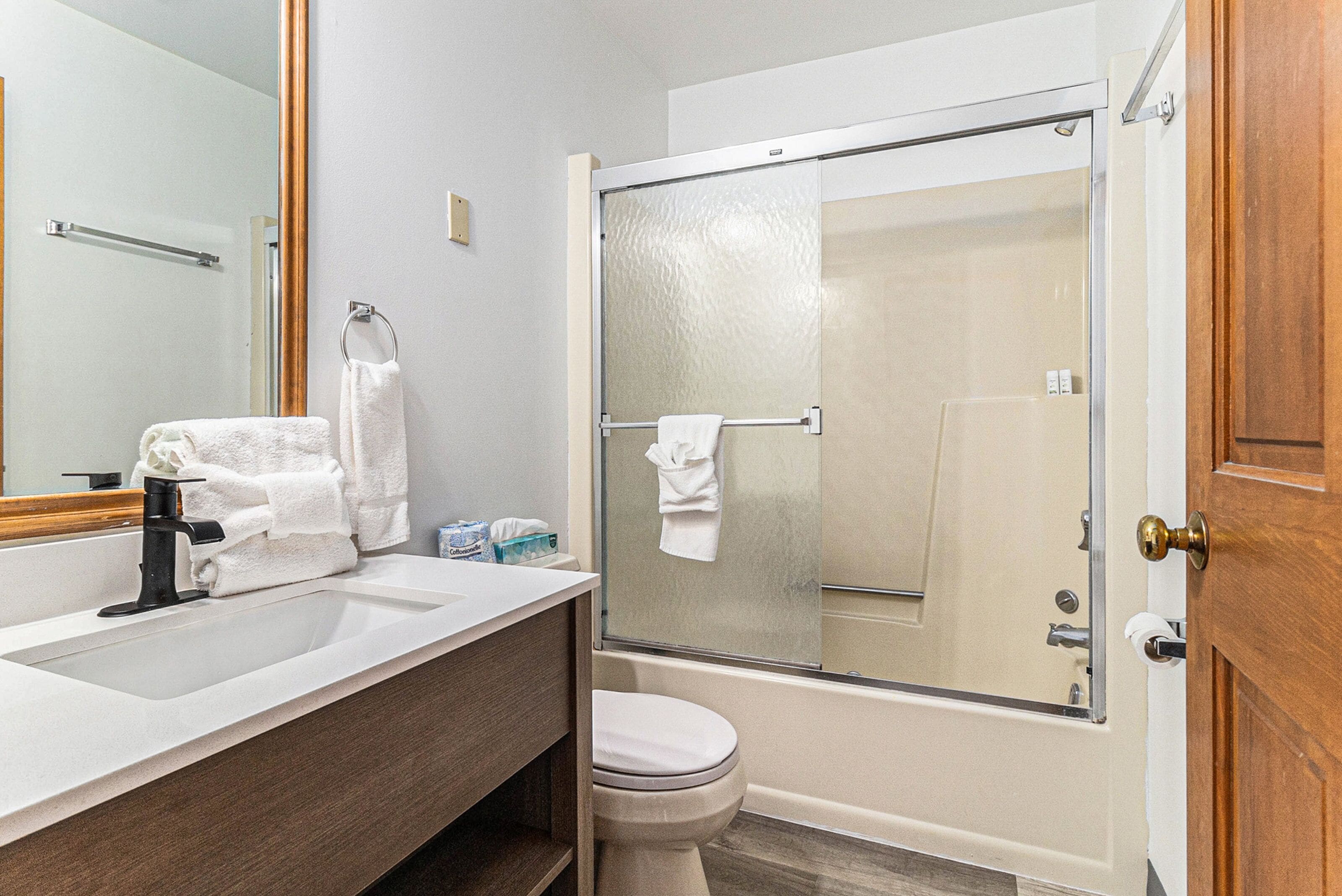 A bathroom with a large mirror, a sink, a toilet, and a glass-enclosed shower.