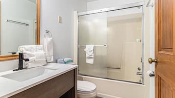 A bathroom with a large mirror, a sink, a toilet, and a glass-enclosed shower.