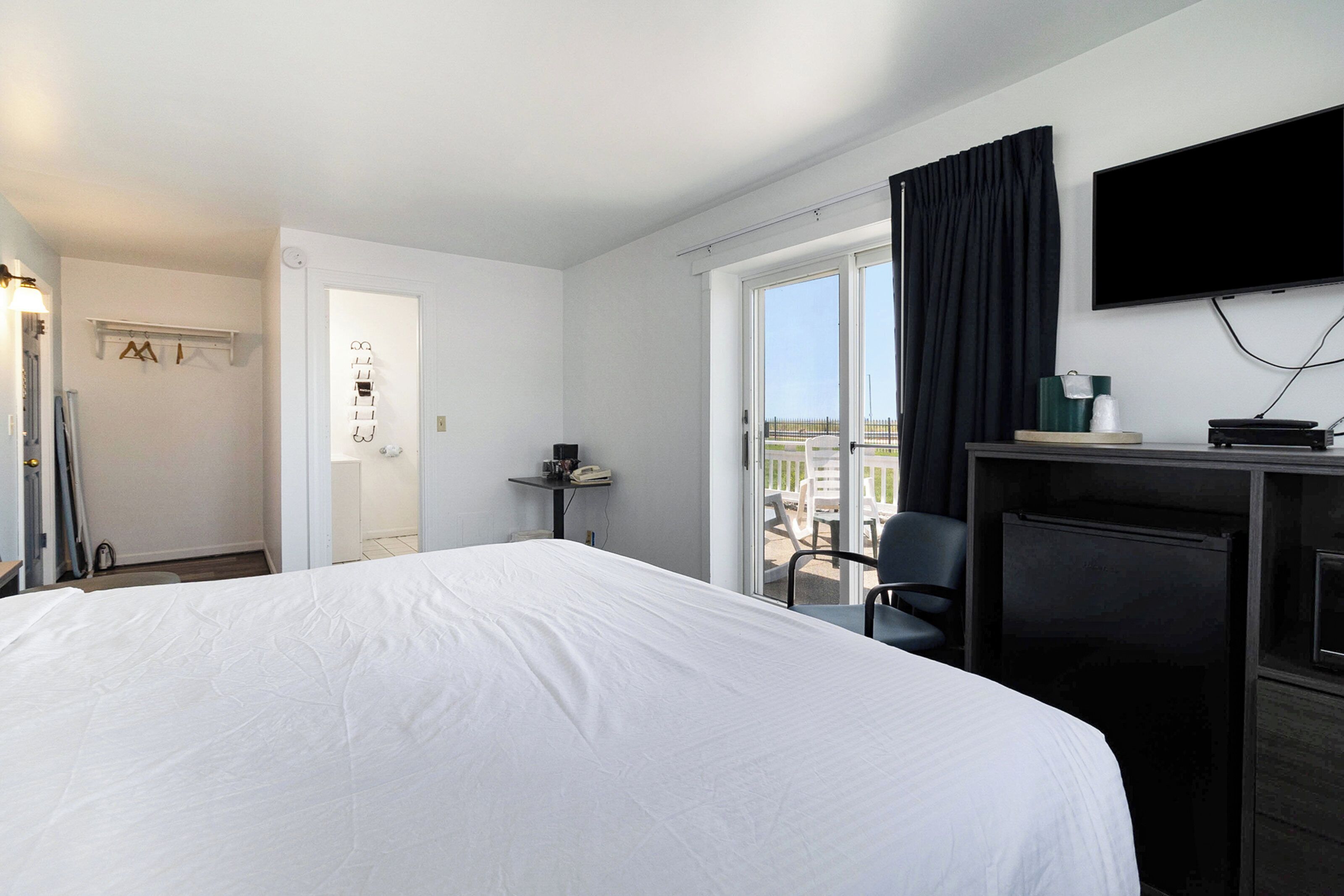 A hotel room with a large bed, a desk with a chair, a television, and a view of the city through the window.