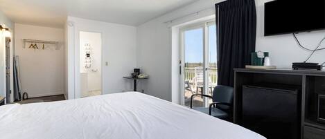 A hotel room with a large bed, a desk with a chair, a television, and a view of the city through the window.
