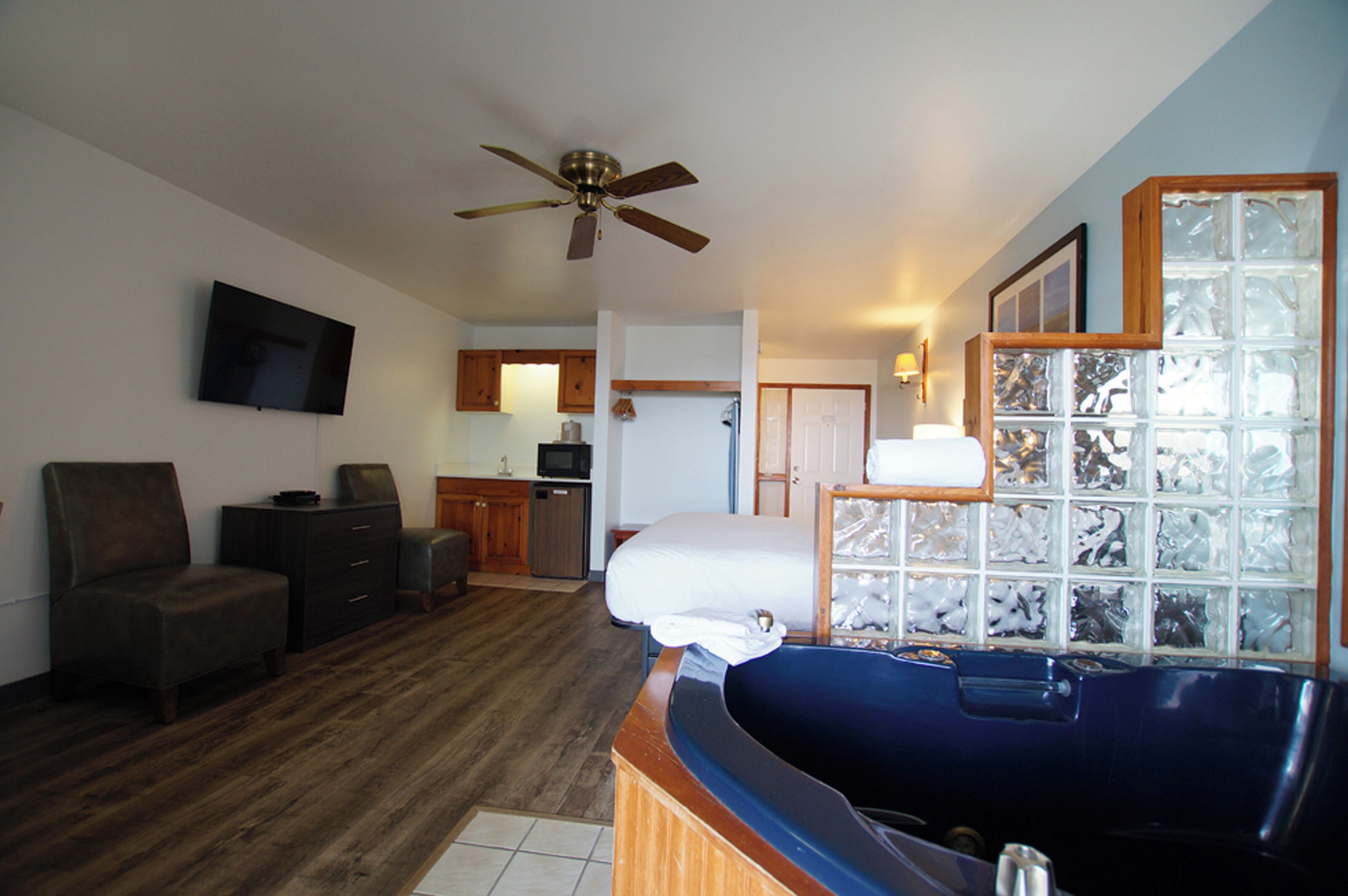 A hotel room with a large bathtub, a ceiling fan, a television, and a kitchen area in the background.