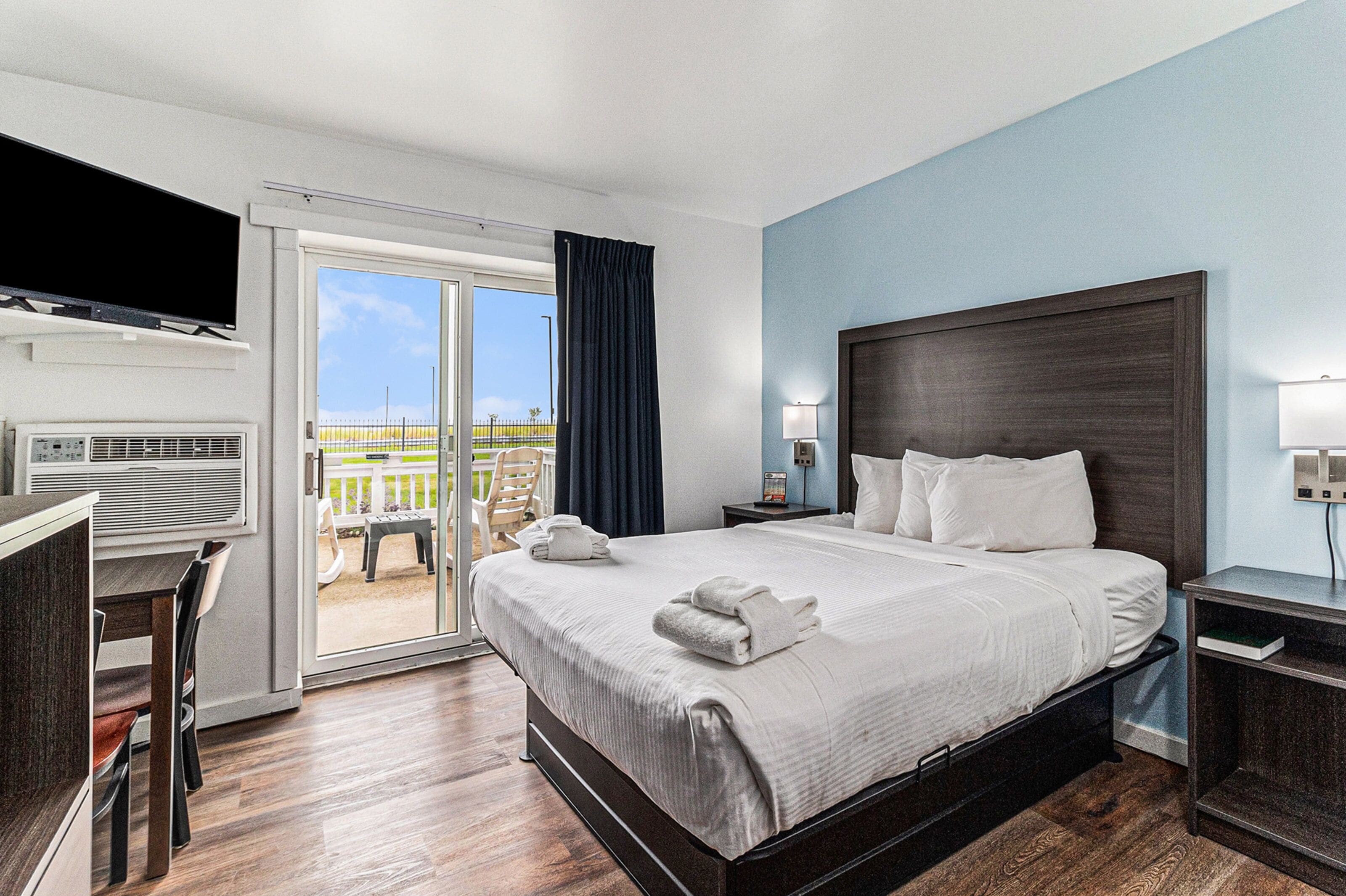 A hotel room with a large bed, a desk, a TV, and a balcony with a view.