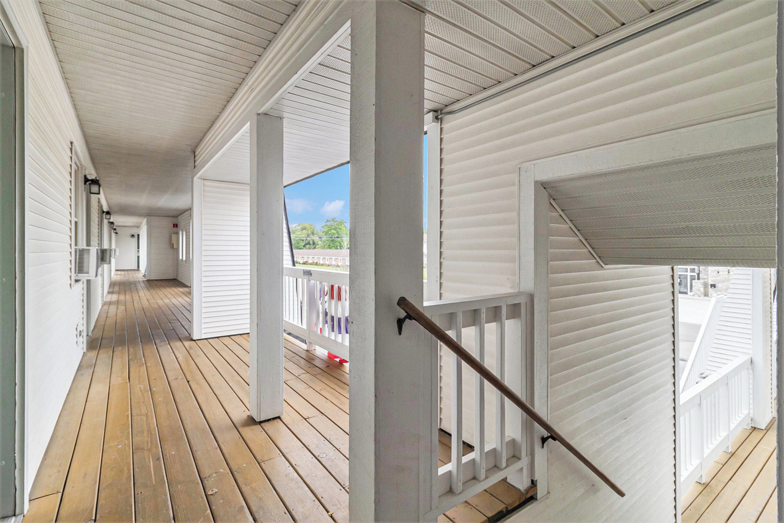 A covered wooden deck with white railings and a staircase.