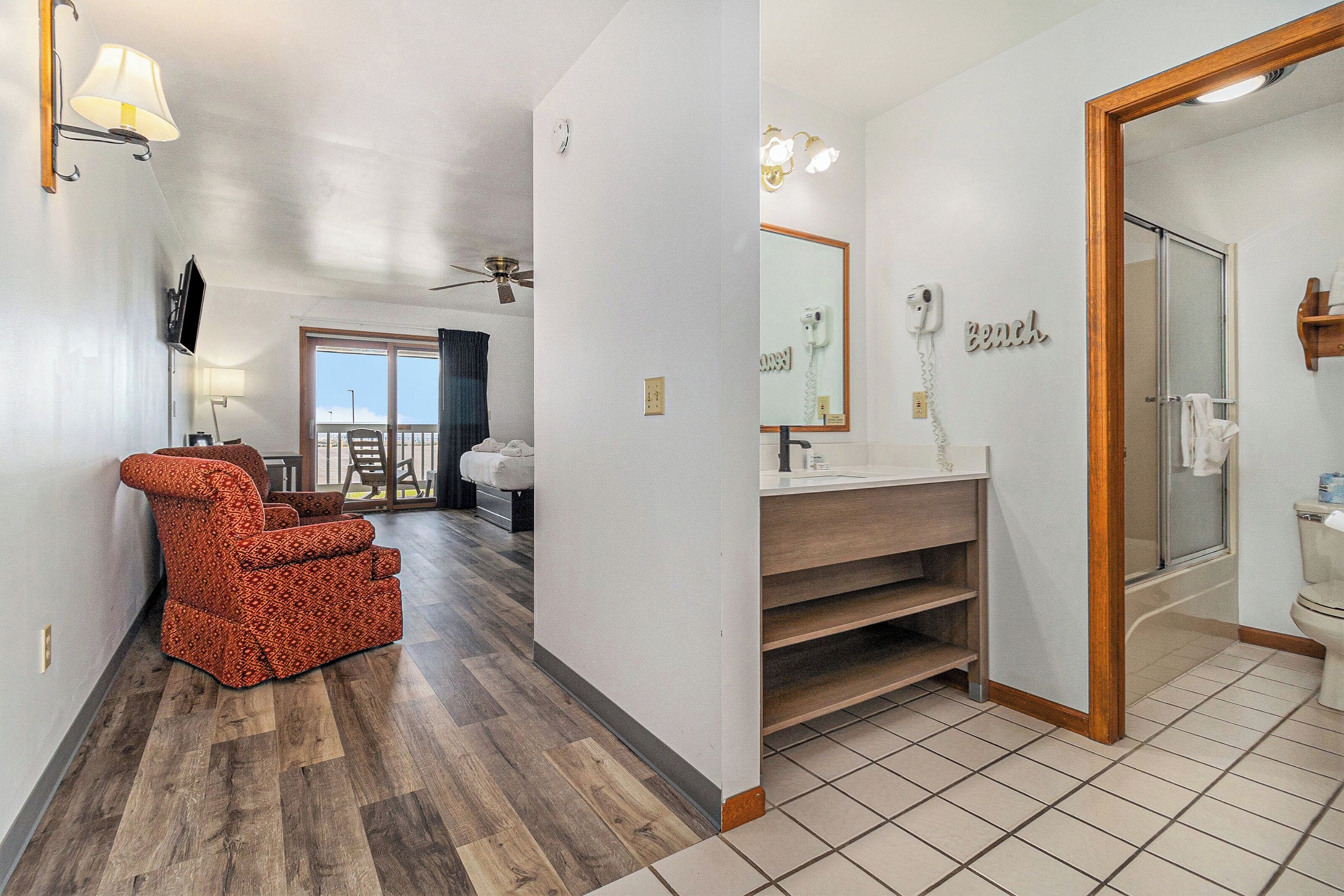 Une chambre d’hôtel avec un plancher en bois, un canapé rouge à motifs, une salle de bain avec douche et un balcon avec vue.