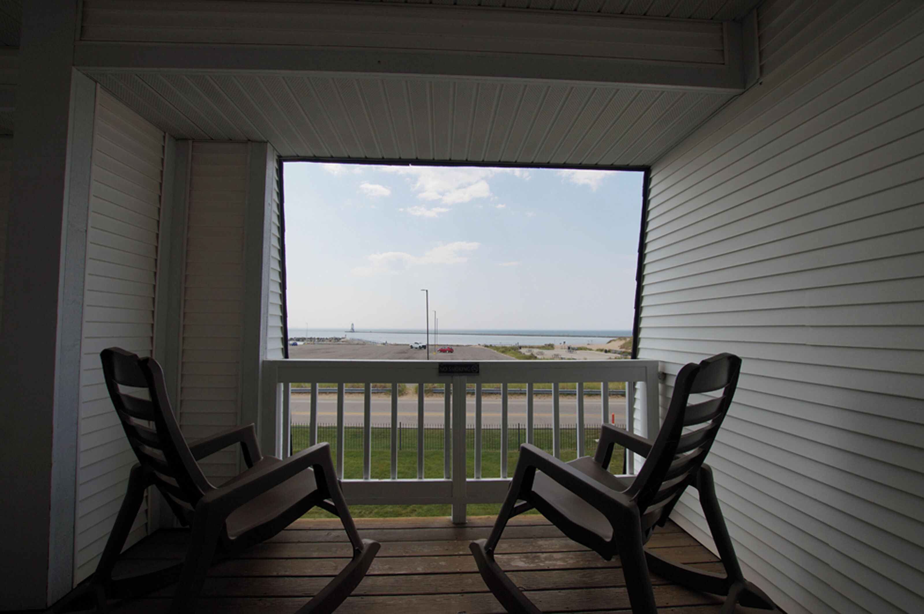 A balcony with two rocking chairs, a view of the beach, and a clear sky.