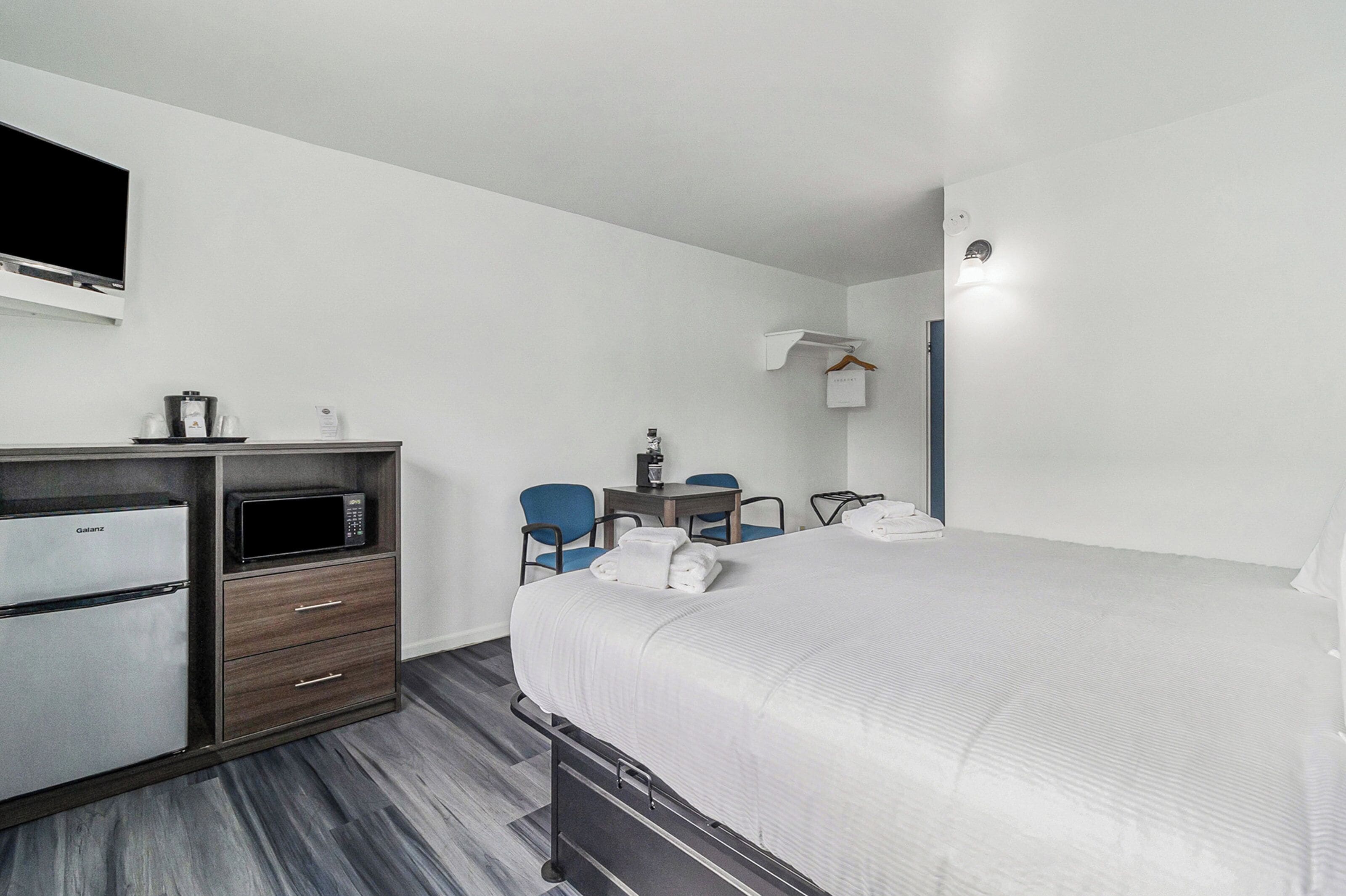 A hotel room with a bed, a desk, a chair, a microwave, and a refrigerator.