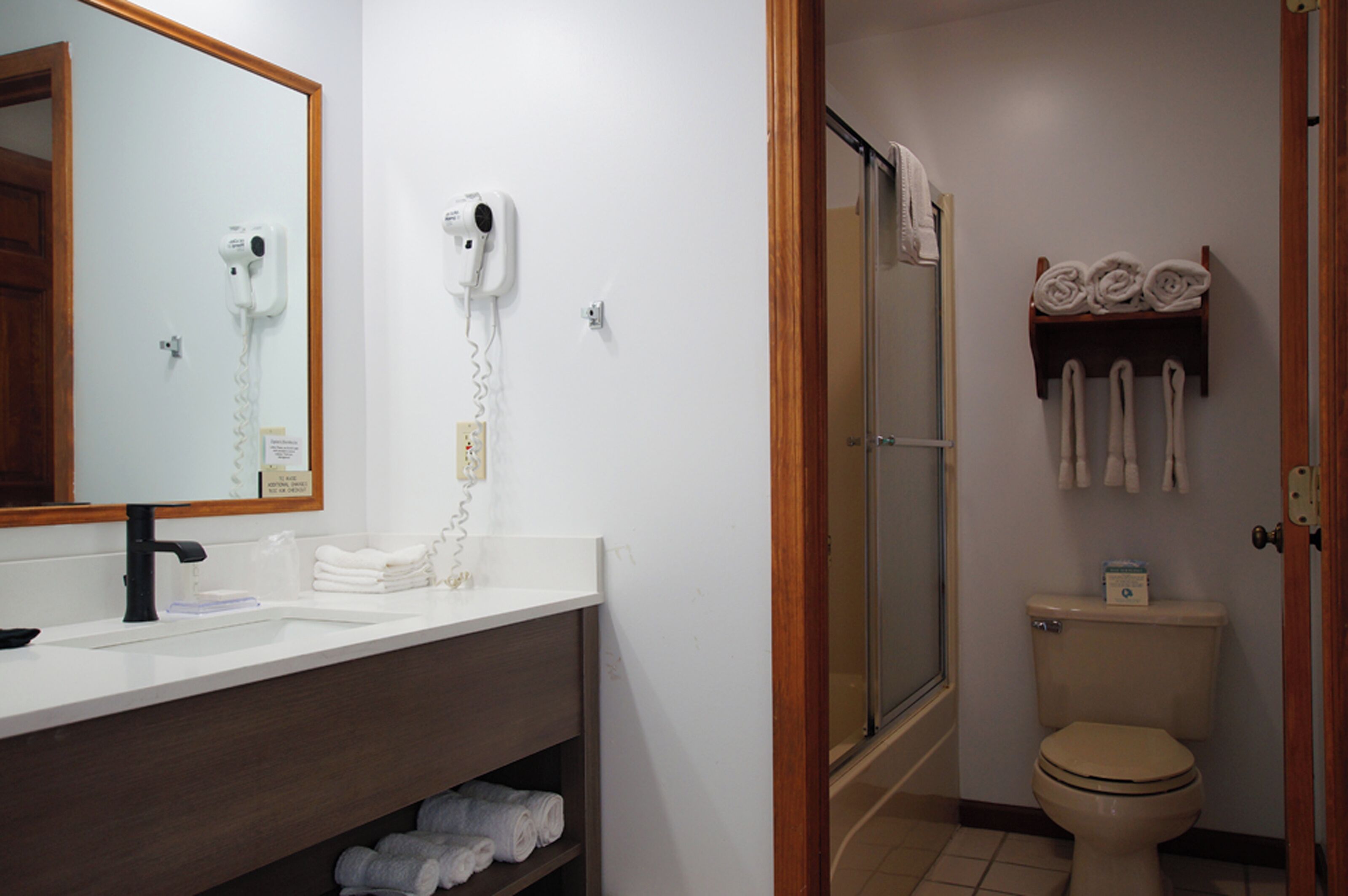 Un bagno con un lavandino bianco, un asciugacapelli montato a parete, un water e una cabina doccia.
