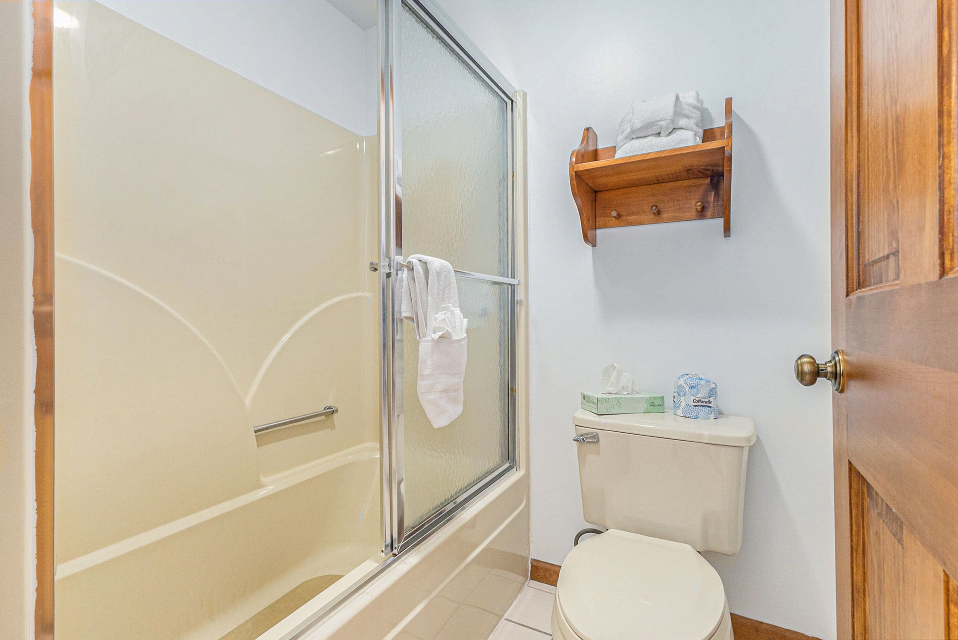Un baño con ducha de vidrio, inodoro y estante de madera con toallas.