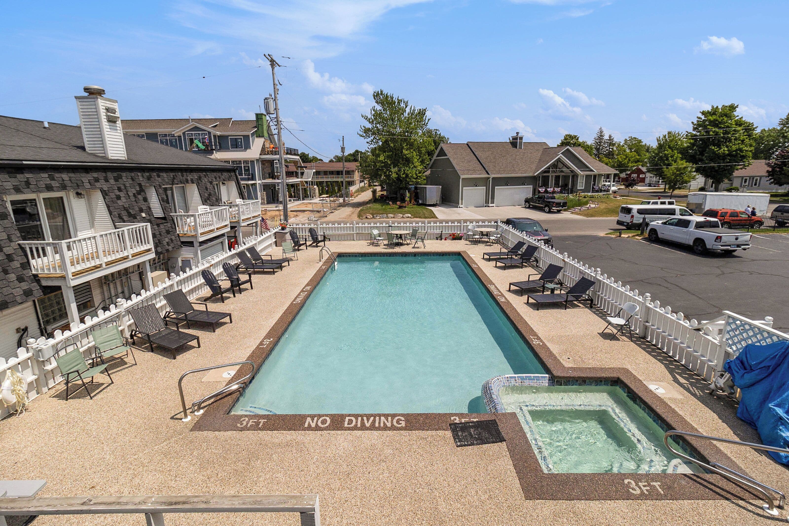 A rectangular swimming pool with a 'NO DIVING' sign, surrounded by lounge chairs and a white fence.