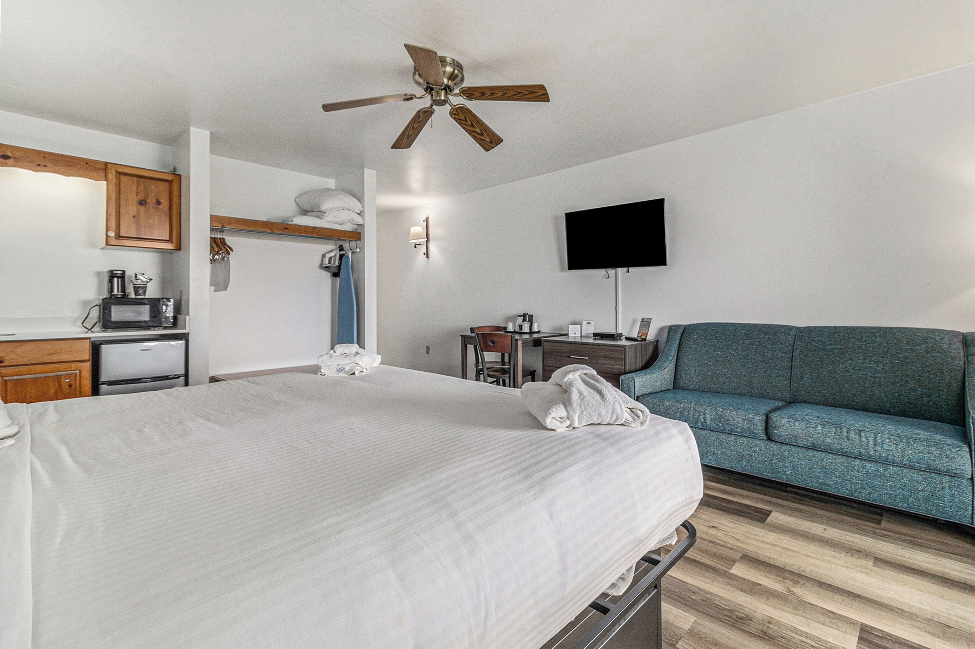 Habitación de hotel con cama, escritorio, silla, televisor y ventilador de techo.