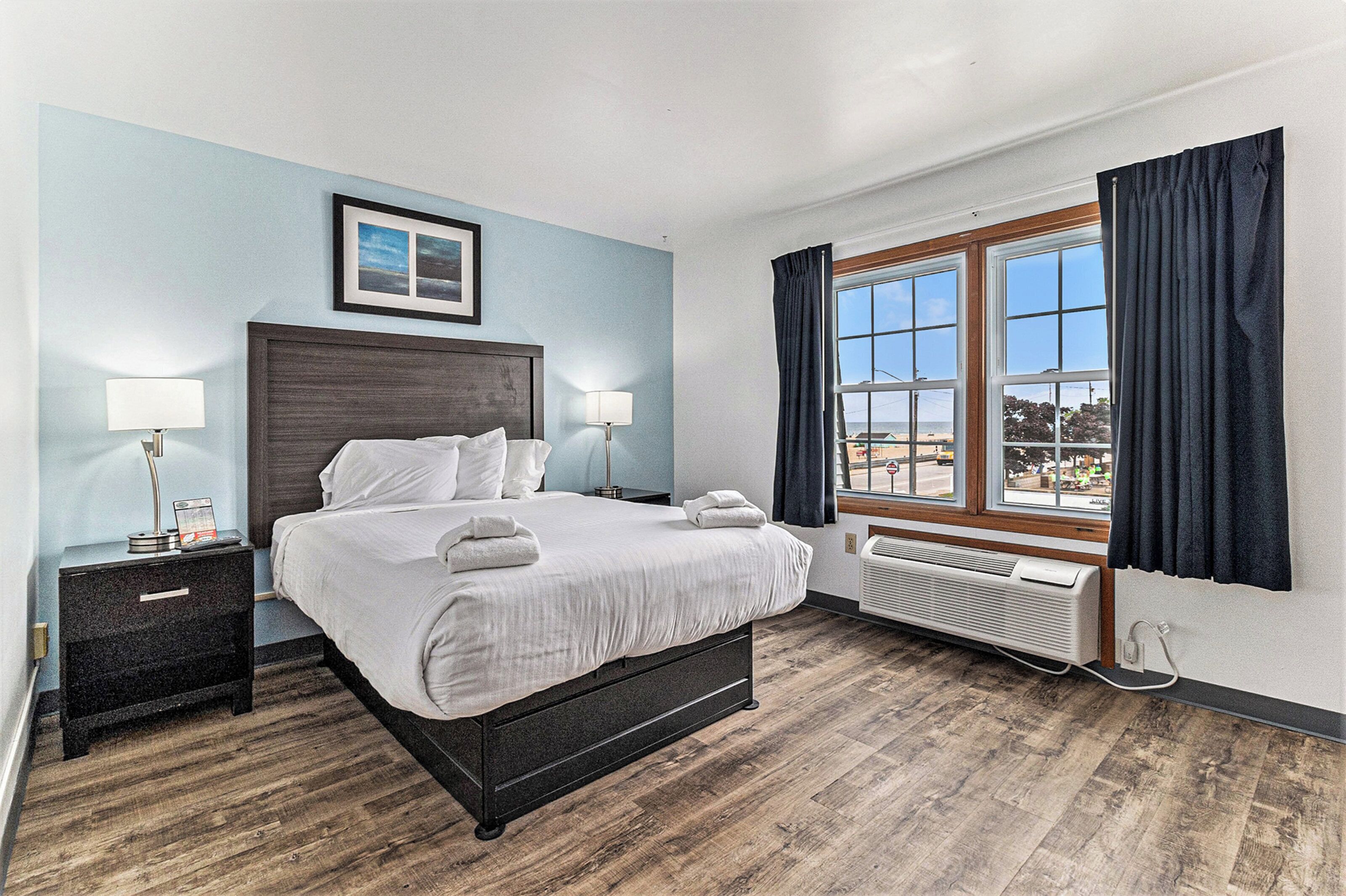 A hotel room with a large bed, bedside tables, a window with curtains, and a view of the cityscape.