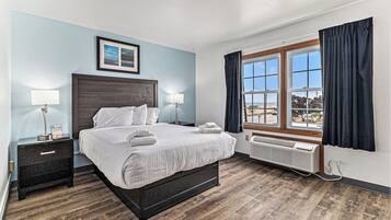 A hotel room with a large bed, bedside tables, a window with curtains, and a view of the cityscape.