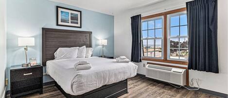 A hotel room with a large bed, bedside tables, a window with curtains, and a view of the cityscape.
