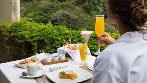 Ein Tisch gedeckt mit Gebäck, einem Glas Orangensaft und einem Martini-Glas, mit Grünpflanzen im Hintergrund.