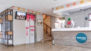 A hotel reception area with a wooden reception desk, a staircase, and a wall with a clock and a logo. - Frida Costa Azul (Mexico City)