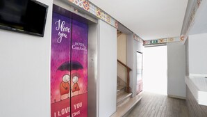 A hotel corridor with a staircase, a TV mounted on the wall, and a colorful door with a romantic illustration. - Frida Costa Azul (Mexico City)
