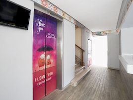 Un corridoio d'albergo con una scala, una TV a parete e una porta colorata decorata con un'illustrazione romantica.