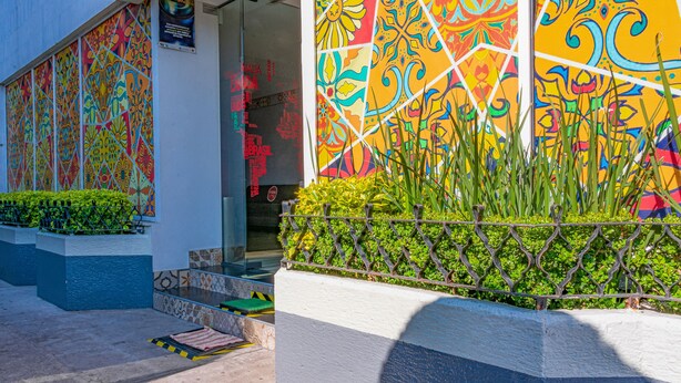 A building facade with colorful geometric patterns, a metal fence, and a small garden area with green plants. - Frida Costa Azul (Mexico City)