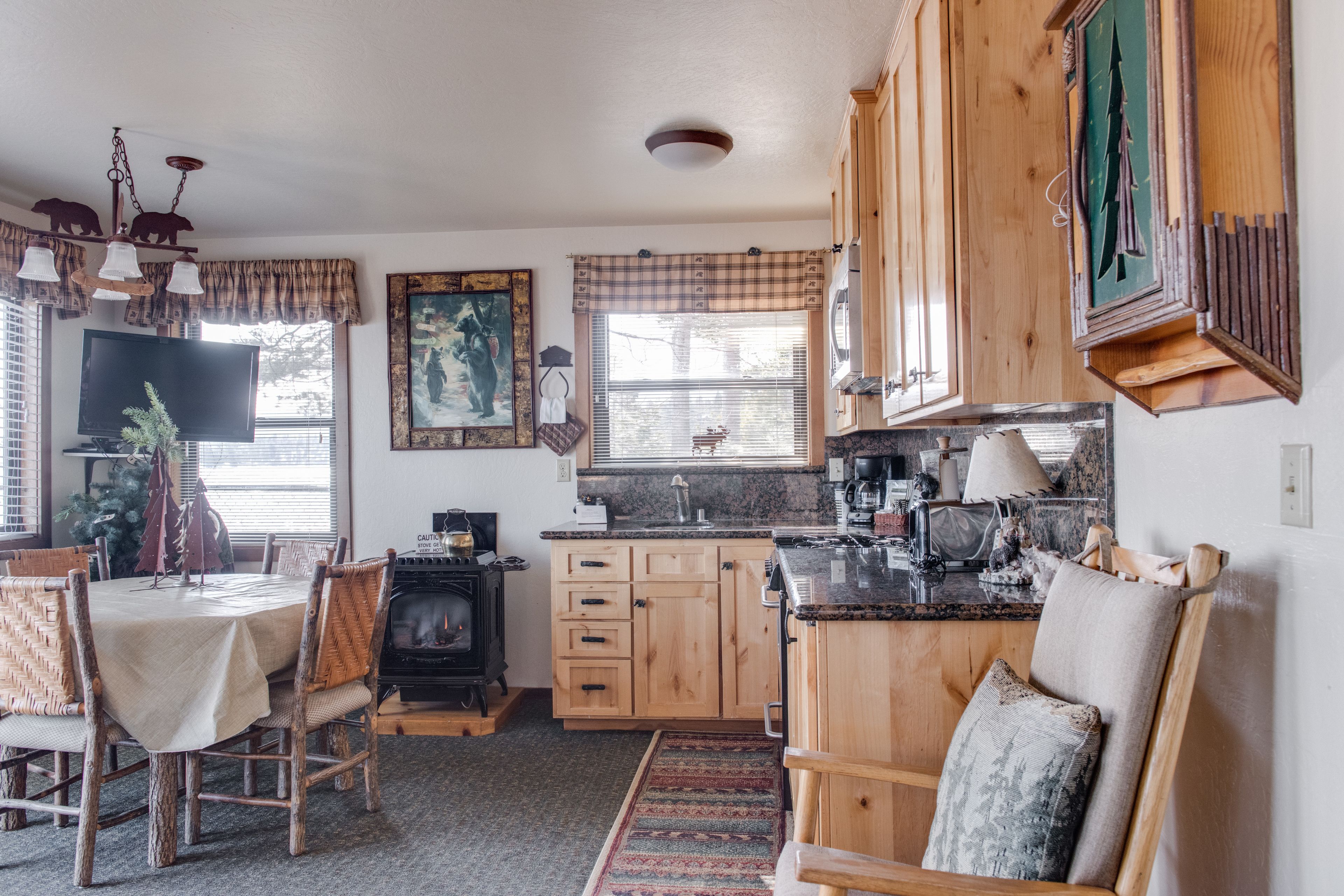 A cozy kitchen with wooden cabinets, a dining area with wicker chairs, and a fireplace.