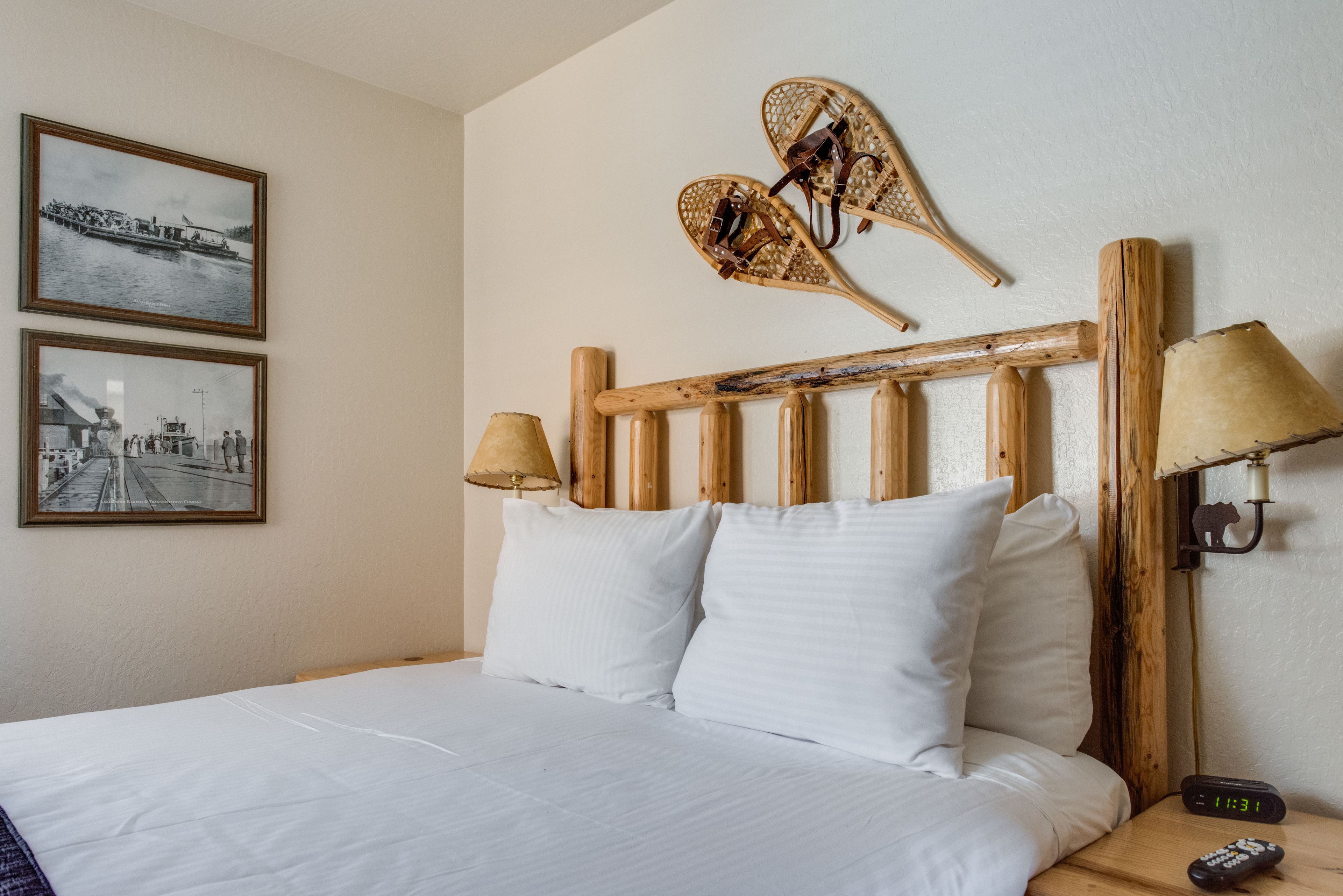 A neatly made bed with white linens, a wooden headboard with two wall-mounted lamps, and two framed photographs on the wall.