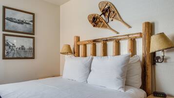 A neatly made bed with white linens, a wooden headboard with two wall-mounted lamps, and two framed photographs on the wall.
