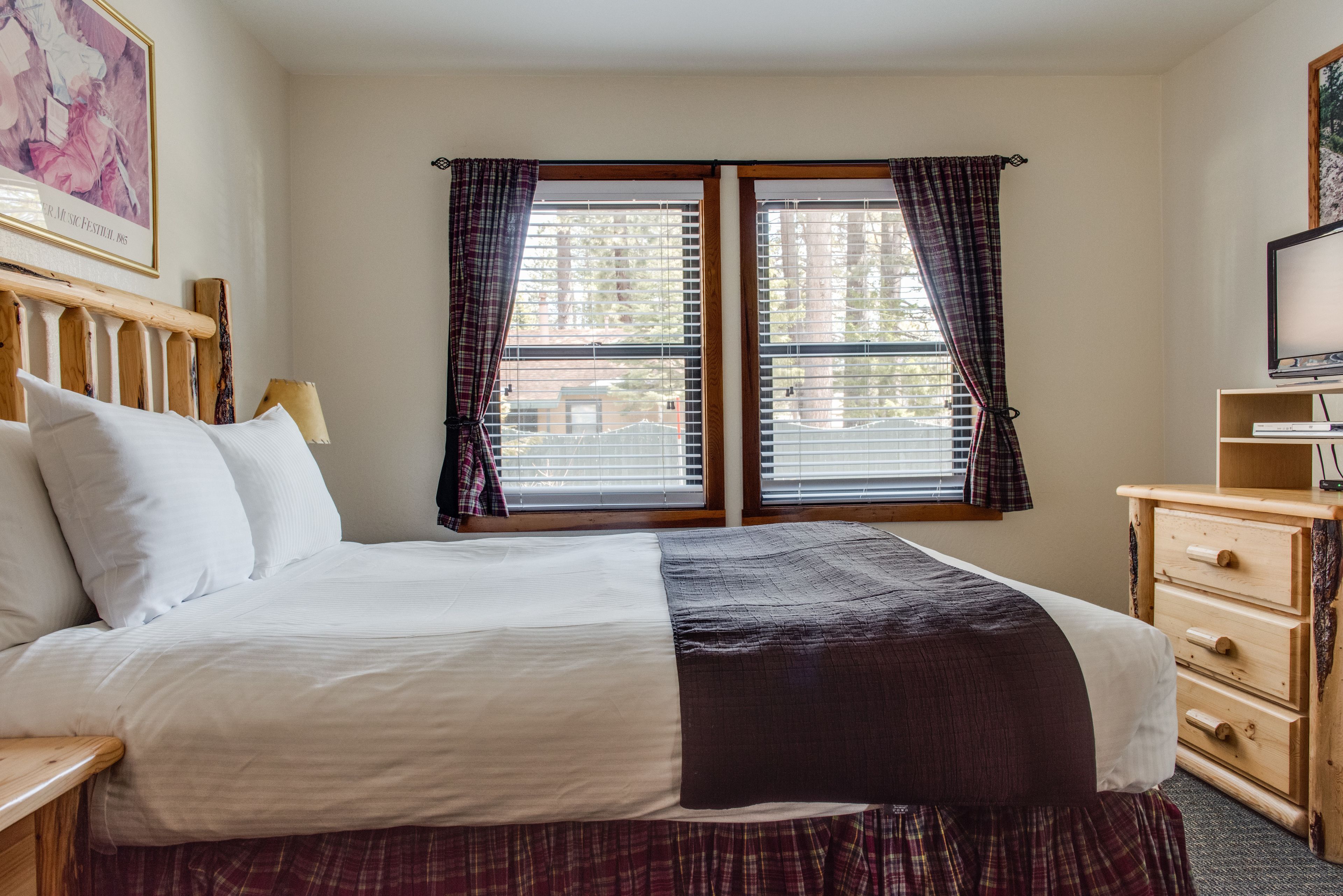 Une chambre d’hôtel avec un lit, une commode en bois, une télévision et une fenêtre avec des rideaux.