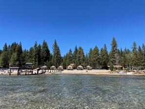 Una proprietà sul lago con acque limpide, una spiaggia sabbiosa e diverse cabine immerse in alte conifere.