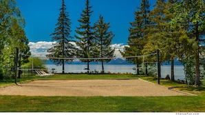 Cancha de voleibol con red, rodeada de árboles y vista al lago.