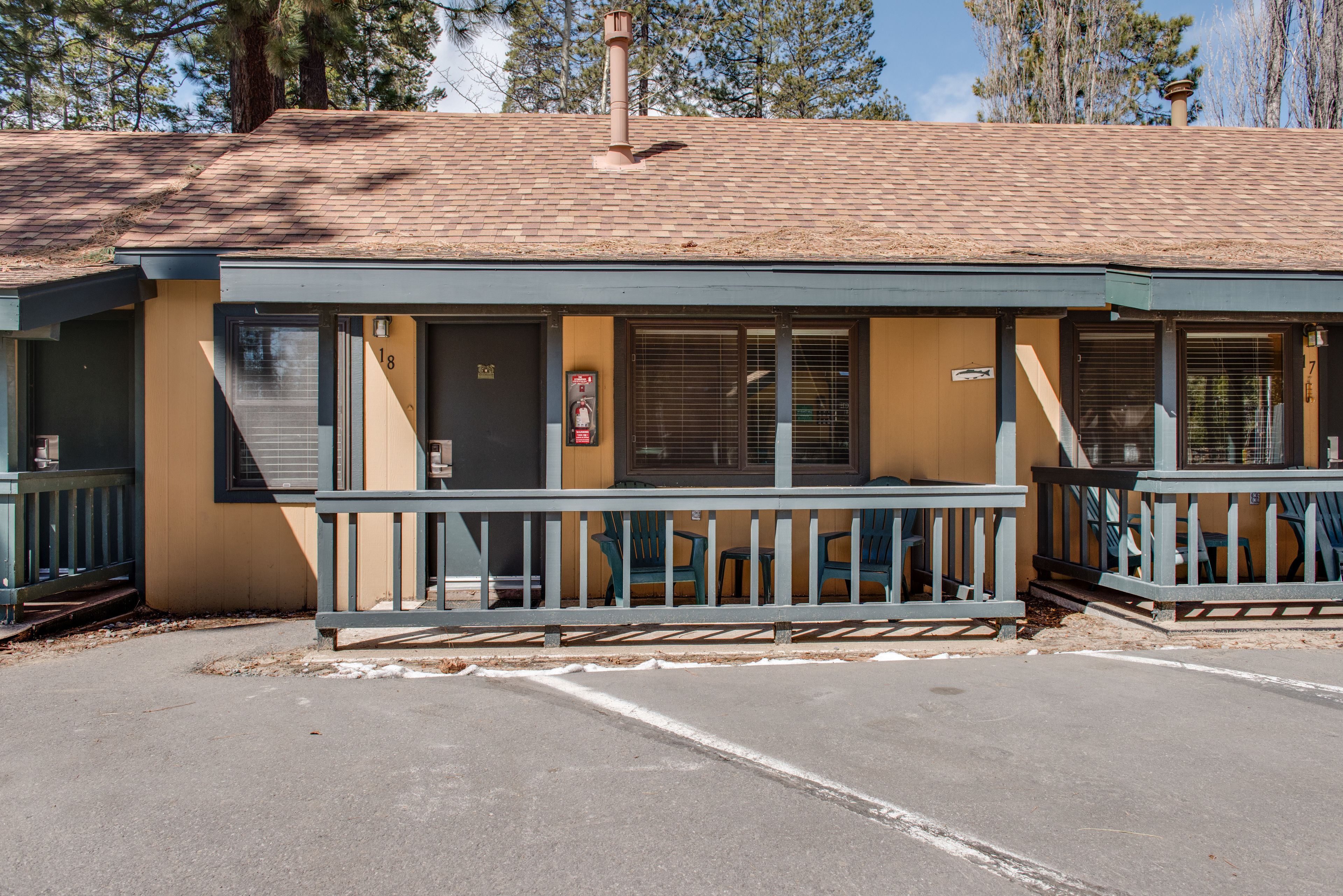 A motel with a covered porch, a parking lot, and a chimney.