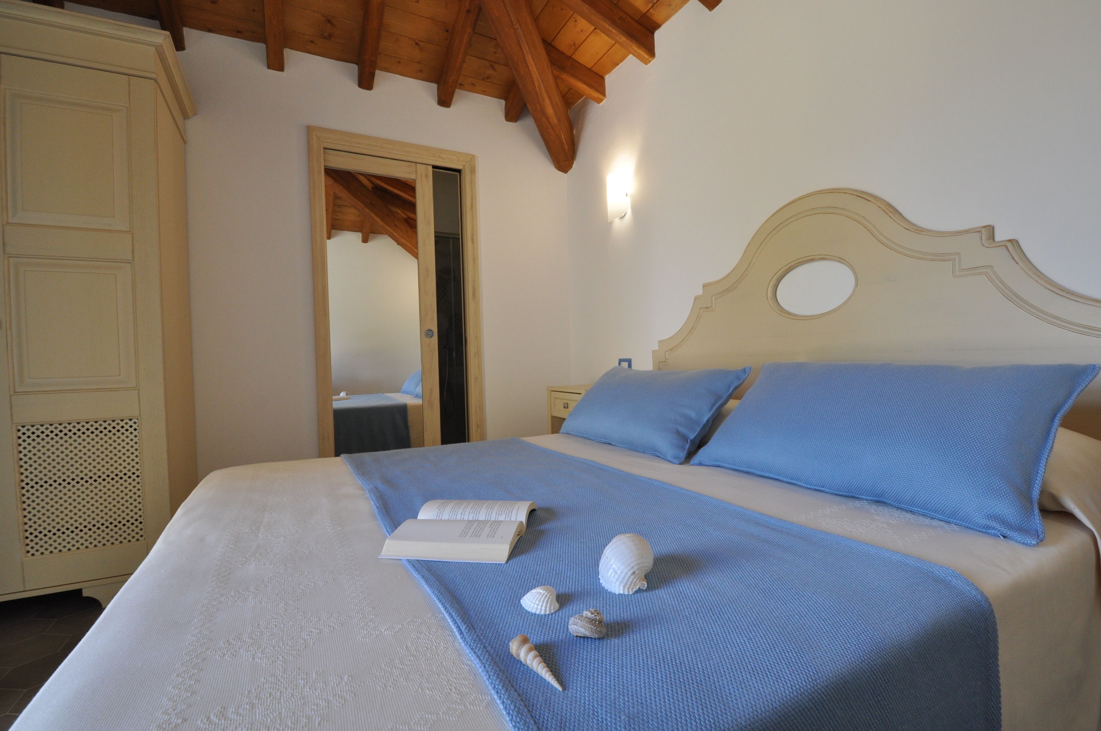 A neatly made bed with a blue bedspread, a book, and seashells on the bed.