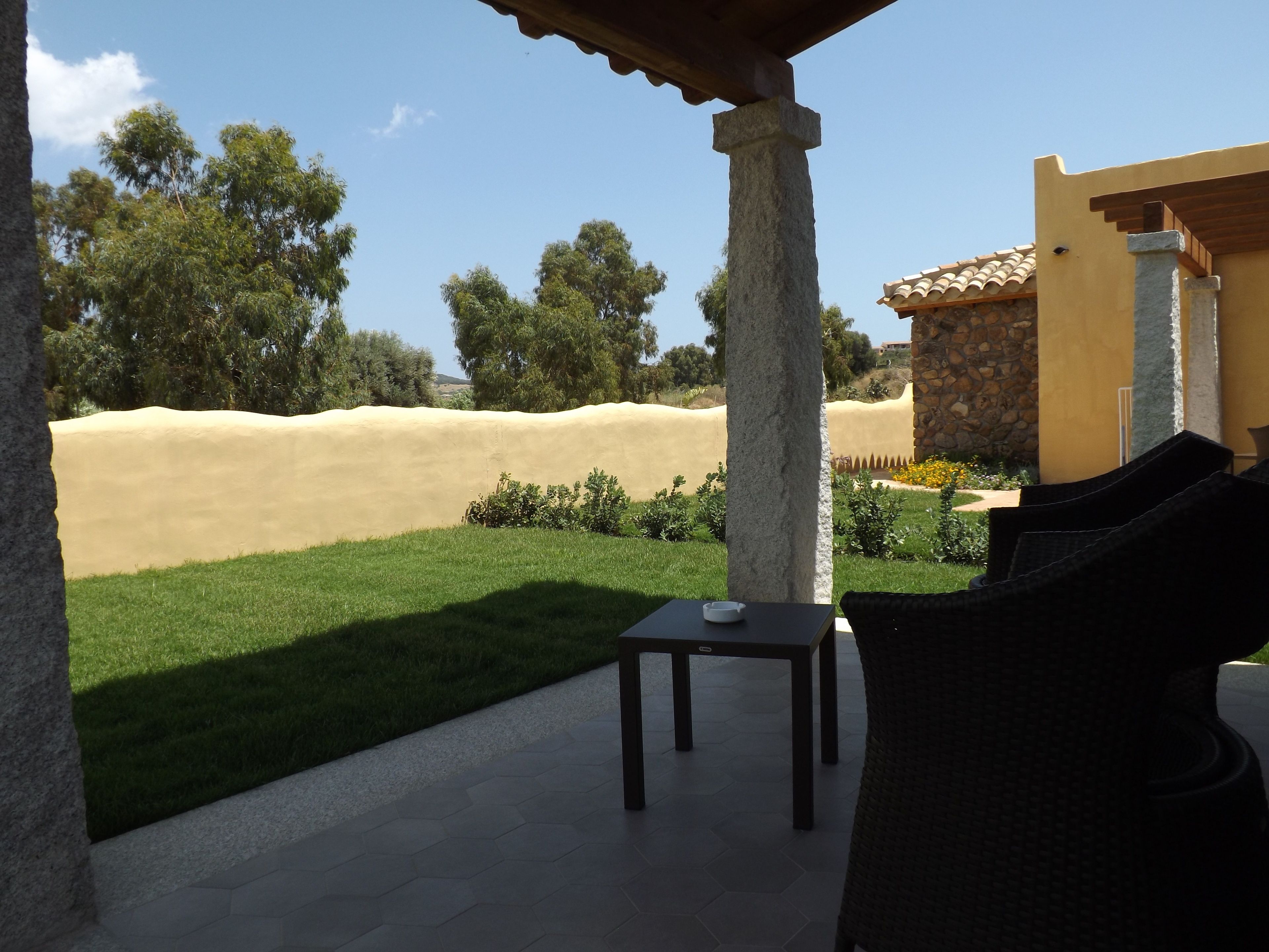 A patio with a table and chairs, a stone wall, and a view of a green lawn and trees.