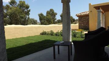 A patio with a table and chairs, a stone wall, and a view of a green lawn and trees.