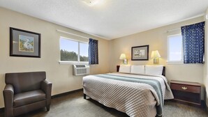 A hotel room with a bed, a chair, a nightstand, and two windows with curtains. - Siegel Select Gautier (Gautier)