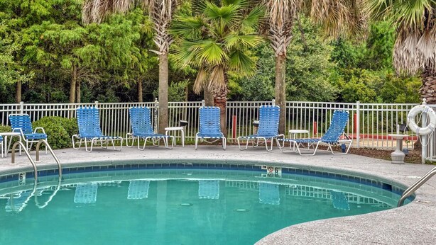 A swimming pool with blue lounge chairs and a white fence. - Siegel Select Gautier (Gautier)
