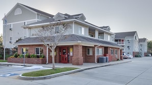 A multi-story hotel with a brick facade, a small front garden, and a parking lot. - Siegel Select Gautier (Gautier)