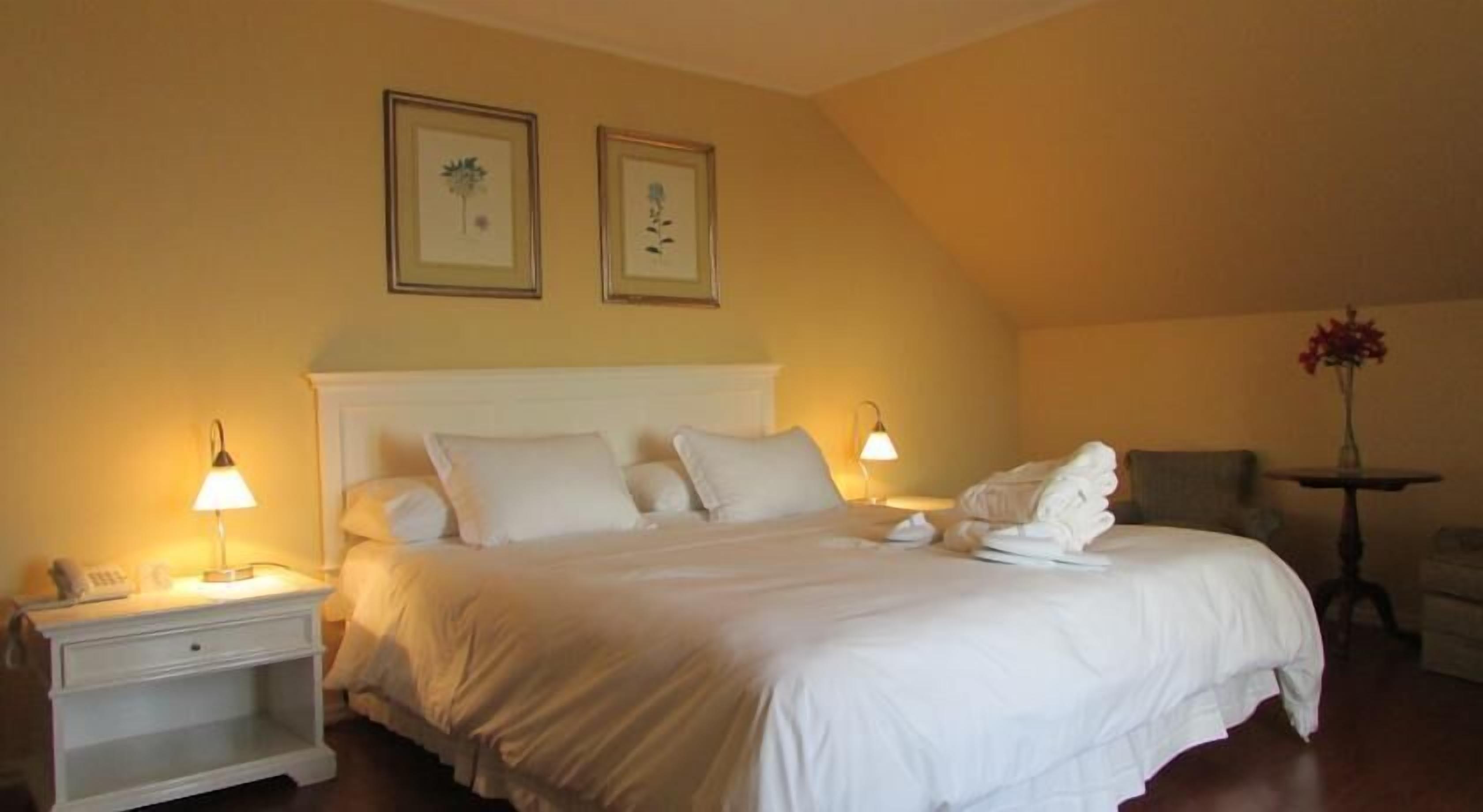 A hotel room with a bed, bedside lamps, a nightstand, a chair, and two framed pictures on the wall.
