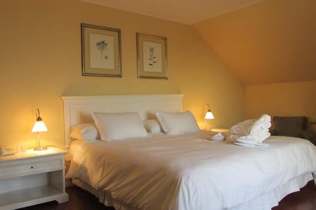 A hotel room with a bed, bedside lamps, a nightstand, a chair, and two framed pictures on the wall.