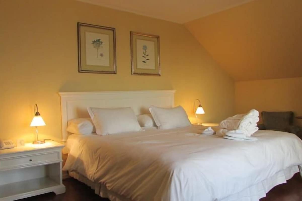 A hotel room with a bed, bedside lamps, a nightstand, a chair, and two framed pictures on the wall.