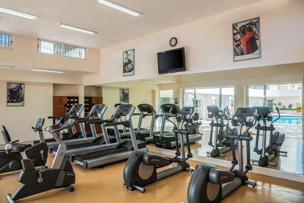 A gym with treadmills, ellipticals, and a pool visible through the glass doors. - Gamma Mérida El Castellano (Mérida)