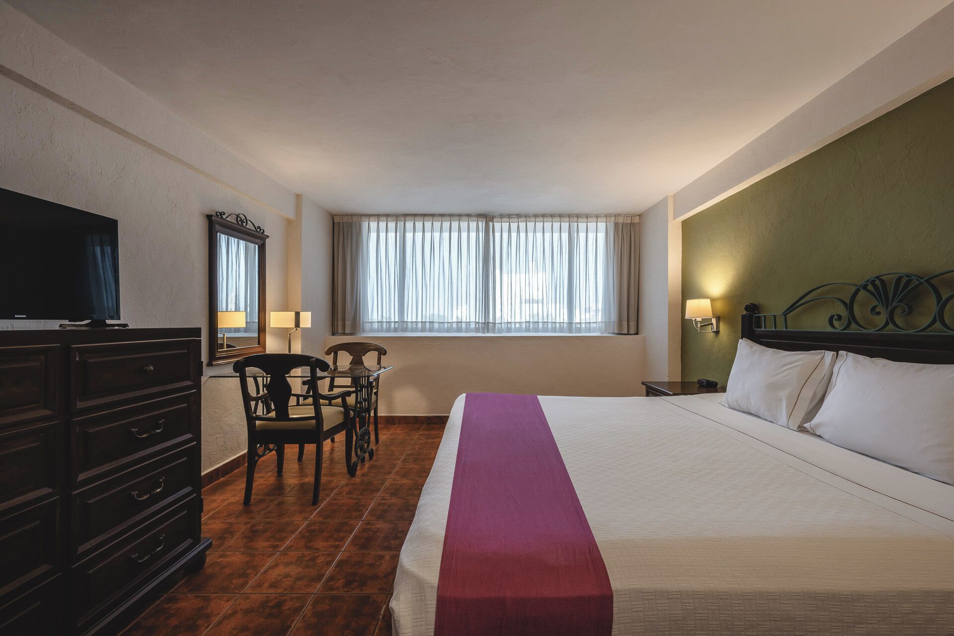 A hotel room with a bed, a desk, a chair, a television, and a window with curtains.